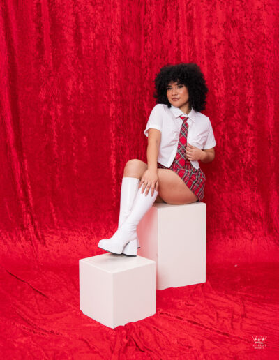 Modelo Brianna en sesión creativa en estudio con vestuario colegial y fondo rojo vibrante